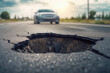A close-up perspective of a road pothole, highlighting the impact of vehicle wheels on the damaged asphalt surface.