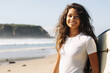 © Surachetsh - Portrait of a smiley young woman with a curly hairstyle carrying a colorful surfboard shot at the sunny day of beach vacation. Generative AI.