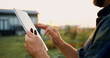 © serg - Businessman promptly carries out online deal to sell crop. Close up of farmers hands using digital computer and searches for information in tablet in agricultural field with plants in windy weather on