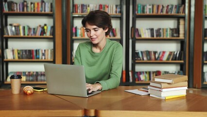 Young girl college student wear green clothes sit at desk use pc laptop computer watching distance online learning seminar class remote university webinar having virtual classroom meeting in library