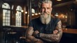 A handsome, bearded, tattooed elderly man stands smiling and looks at the camera. Freelance designer