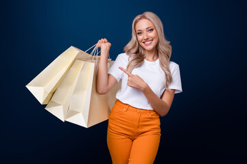 Sticker - Photo of lovely cheerful girl dressed white trendy clothes showing purchase packs isolated on dark blue color background