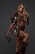 © Fxquadro - An impressive portrait of a strong, blonde barbarian or Viking woman in light leather armor, featuring fur and a bare chest. She confidently wields two axes on a gray backdrop
