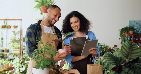 Two professional florists man and woman working at plants using digital tablet computer in flower shops. Teamwork and collaboration with happy co-workers in greenhouse. Two successful colleagues