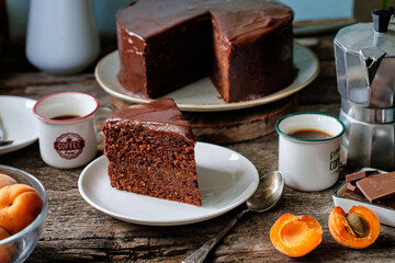 Sticker - Chocolate cake with chocolate icing with apricot jam and cream inside. wooden background, side view