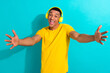 Photo of cheerful excited guy wear yellow t-shirt listening earphones songs having fun isolated teal color background