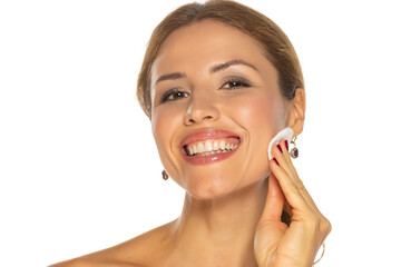 Wall Mural - Close up beauty portrait of a young attractive smiling woman cleaning her face with a cotton pad isolated over white background