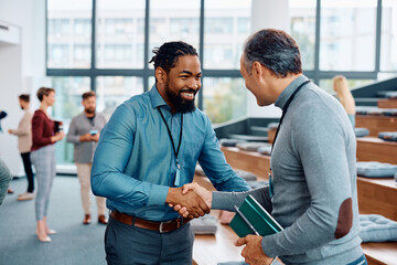 Happy black businessman shaking hands with presenter during education event at conference hall.