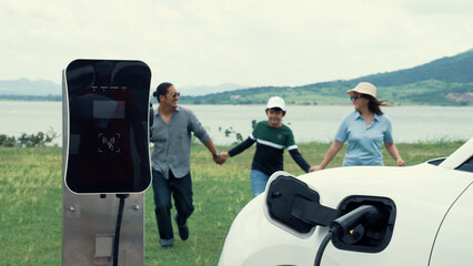 Sticker - Concept of progressive happy family enjoying their time at wind farm with electric vehicle. Electric vehicle driven by clean renewable energy from wind turbine generator for charging station.