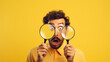 portrait of handsome young man with magnifying glass looking at camera on yellow background