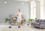 Young sporty man in homewear doing stretching exercises with rubber band in the living room at home. Athletic guy enjoy exercising. Fitness, workout sport and home training concept.