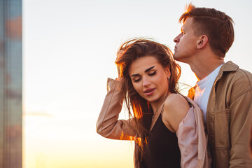 Wall Mural - Young loving couple on a surprise date on rooftop on Saint Valentine's Day. Laughing, kissing embracing, drinking wine, having candlelit picnic with cityscape urban view with skyscrapers on background