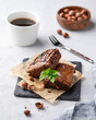 Pieces of chocolate brownies with hazelnuts and salted caramel on baking paper on a light background with a cup of coffee. The concept of delicious and sweet homemade pastries for breakfast.