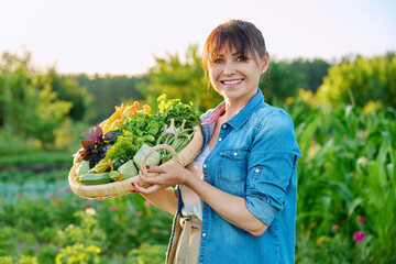 Wall Mural - Smiling woman with basket of fresh green vegetables and herbs on farm