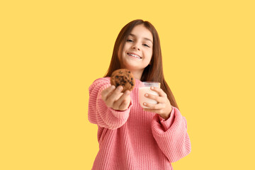 Wall Mural - Happy little girl holding sweet chocolate cookie and glass of fresh milk on yellow background