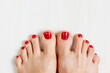 Beautiful woman's vinous burgundy nails with beautiful pedicure. Female feet with bright pedicure on white wooden background. Autumn and winter concept. Top view, copy space, horizontal, close up