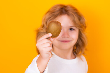 Wall Mural - Vitamin and healthy fruits for kids. Child hold kiwi in studio. Kiwi fruit. Studio portrait of cute kid boy with kiwi isolated on yellow.