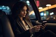 Beautiful young business woman smiling and using smartphone inside the car while traveling during a night. Contacting friends or business associates when you are away.
