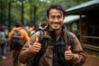 © Alina Zavhorodnii - A male traveller with a backpack and wearing mackintoshes points two fingers up and smiles in the background of a group of tourists
