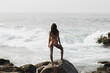 © Buyanskyy Production - Spectacular view of a beautiful bikini woman model with an amazing slim body standing on a rocky cliff and looking at the sea. An epic scene with stormy waves and a gorgeous woman model