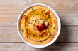 Roasted red pepper hummus in white bowl on wooden table. Top view