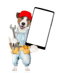 Poster - Funny puppy wearing red cap and denim overalls with tool belt holding wrench and showing big smartphone with white blank screen in it paw. Isolated on white background