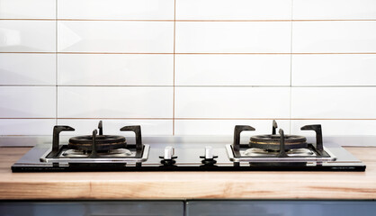 Front view of Contemporary tempered glass gas stove hob with Two burners with auto ignition knob on wooden countertop, cast iron pan supports fan hood and oven built in compact