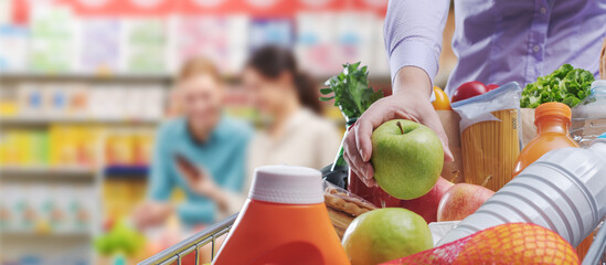 Wall Mural - Woman putting groceries in the shopping cart