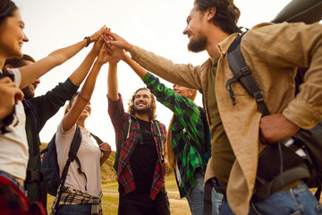 Team of happy friends go on hike and give each other high five. Group of active cheerful positive male female tourists with backpacks, motivated to reach goal. Travel, teamwork, fun, adventure concept