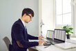 © Studio Romantic - Young professional Caucasian man accountant wearing glasses uses calculator to prepare company's tax returns or conduct business audit sits at office table with laptops in front of window