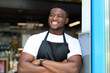 Confident and cheerful young entrepreneur, the owner of a restaurant, standing with crossed arms, showcasing a welcoming and professional demeanor.