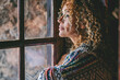 One alone woman standing at home near the window looking outside and thinking. Single female people lifestyle. Waiting friends and thoughts. Young lady indoor leisure. Side portrait of middle age