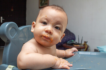 Wall Mural - Beginning of complementary nutrition. 6 month old baby eating guava porridge. Child has fun with face full of food