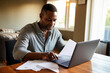 © AI_images - Black man with disability checking his medical documents and filling form on laptop