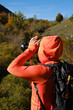 Photographer into the woods taking picture with orange technical mountain outfit in autumn mood.
