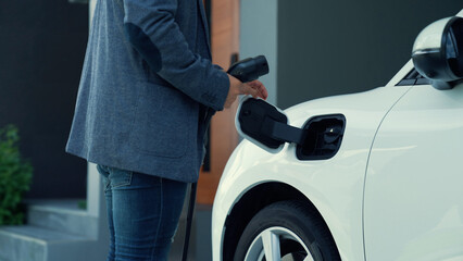 Progressive man attaches an emission-free power connector to the battery of electric vehicle at his home. Electric vehicle charging via cable from charging station to EV car battery