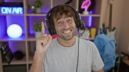 Canvas Print - Confident young man, a gaming number one, in a dark room, pointing a finger with a happy face. wearing headphones, he poses a smart question, lit up with a new idea!