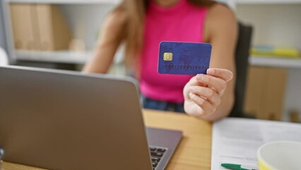 Wall Mural - Confident young hispanic woman enjoying her successful business life, shopping online with credit card at her elegant office workspace, all while working on her laptop.