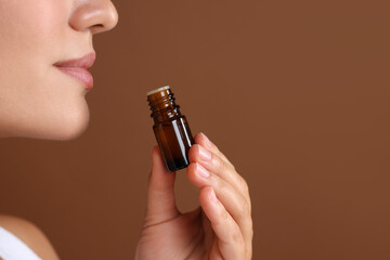 Wall Mural - Woman with bottle of essential oil on brown background, closeup. Space for text