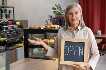 Wall Mural - Smiling business owner holding open sign and inviting to come into her cafe, space for text