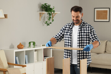 Canvas Print - Man assembling wooden furniture in living room. Space for text