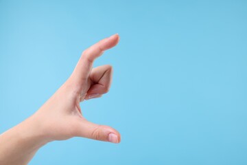 Wall Mural - Woman holding something in hand on light blue background, closeup. Space for text