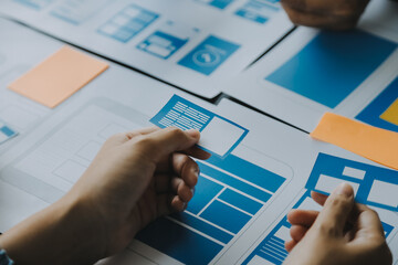 Close up ux developer and ui designer brainstorming about mobile app interface wireframe design on table with customer breif and color code at modern office.Creative digital development agency