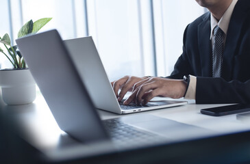 Poster - Asian business man working on laptop computer at modern office. Businessman in black suit working and typing on laptop keyboard, surfing the internet with digital tablet on office table