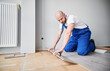 © anatoliy_gleb - Male construction worker laying laminate wooden plank on floor underlayment. Man in work overalls kneeling down by the wall and installing laminate flooring in living room. Home renovation concept.