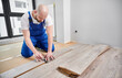 © anatoliy_gleb - Man in work overalls using metal construction ruler and pen while drawing line on laminate flooring board. Male floor installer preparing laminate plank for installation in apartment under renovation.