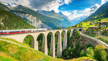 Train Moves On Railroad Bridge In Mountain, Spring Landscape. Switzerland. Red Train Of Bernina Express On Railroad Bridge In Mountains.