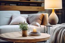 Close up of round glass jar with burning candle on rustic wooden coffee table. Lamp on side table near grey sofa. Minimalist loft home interior design of modern living room.