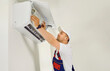 © Studio Romantic - Service and maintenance of air conditioner. Male technician is cleaning and replacing air conditioner filter that hangs on wall inside house. Man inserts new internal air conditioner filter.