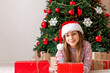 the girl opens gifts. a girl with blond hair in a red hat unpacks surprises, a Christmas tree in the background. christmas concept